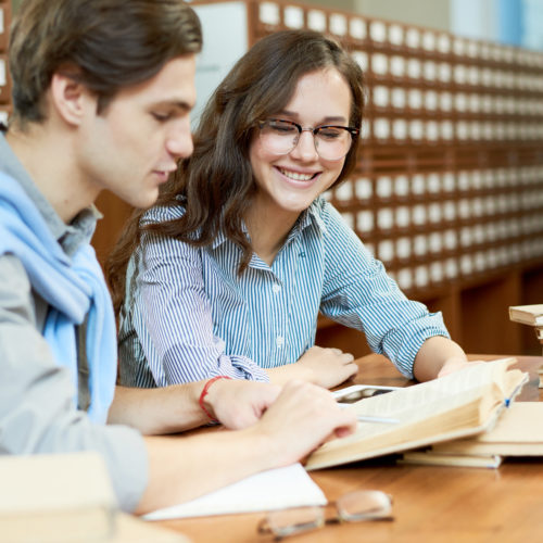 Cheerful content student friends learning from book and knowing new information in preparation for exam in college library